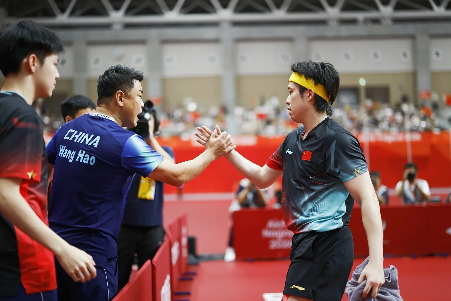 Wang Chuqin shares a high-five with coach Wang Hao and teammates.